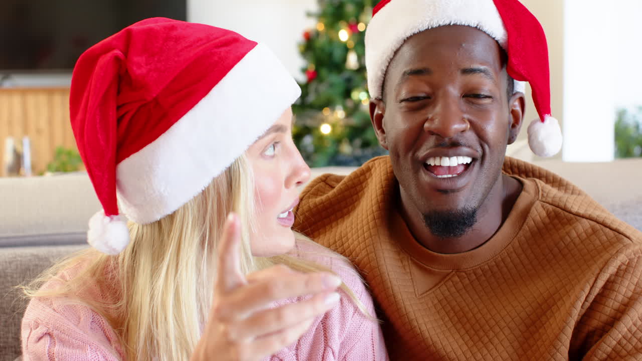 diverse couple wearing Santa hats smiling joyfully at home during Christmas