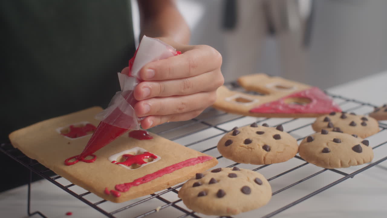 Unrecognizable Kid Decorating Gingerbread House with Red Glaze