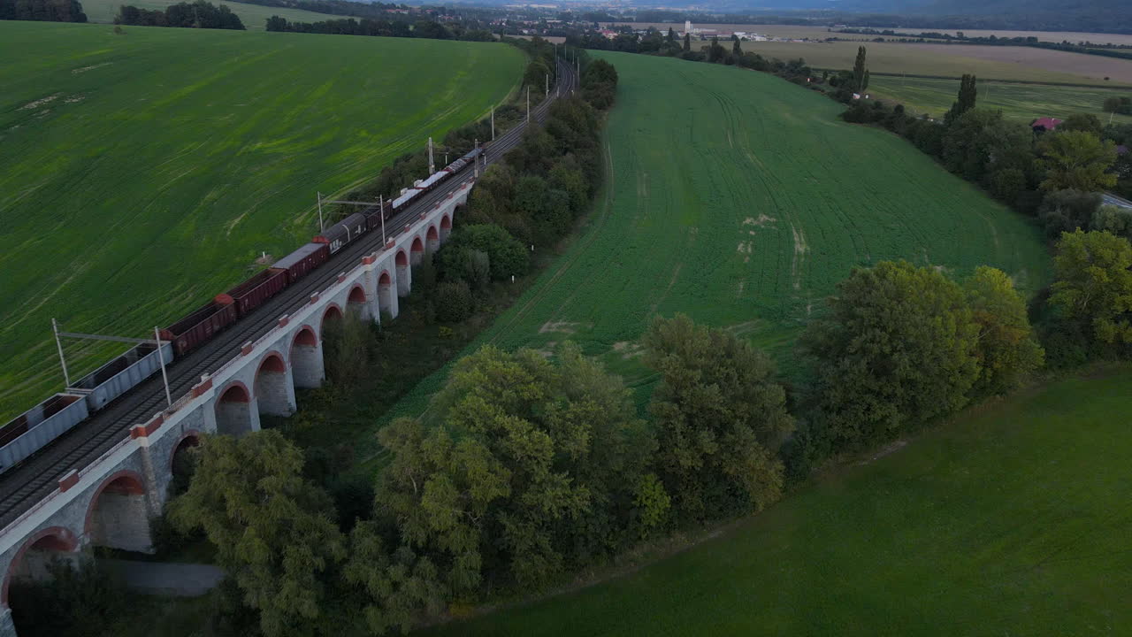 vista aérea de un viaducto de tren con un tren que pasa y el campo circundante en el fondo