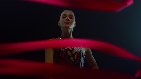 girl practicing rhythmic gymnastics. gymnast with ribbon looking camera indoors