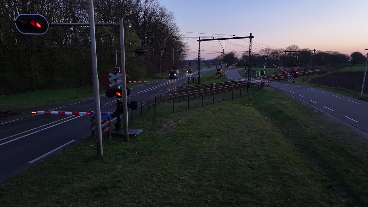 Closed train tracks moment while the road crossing them on evening light and signal light visible.