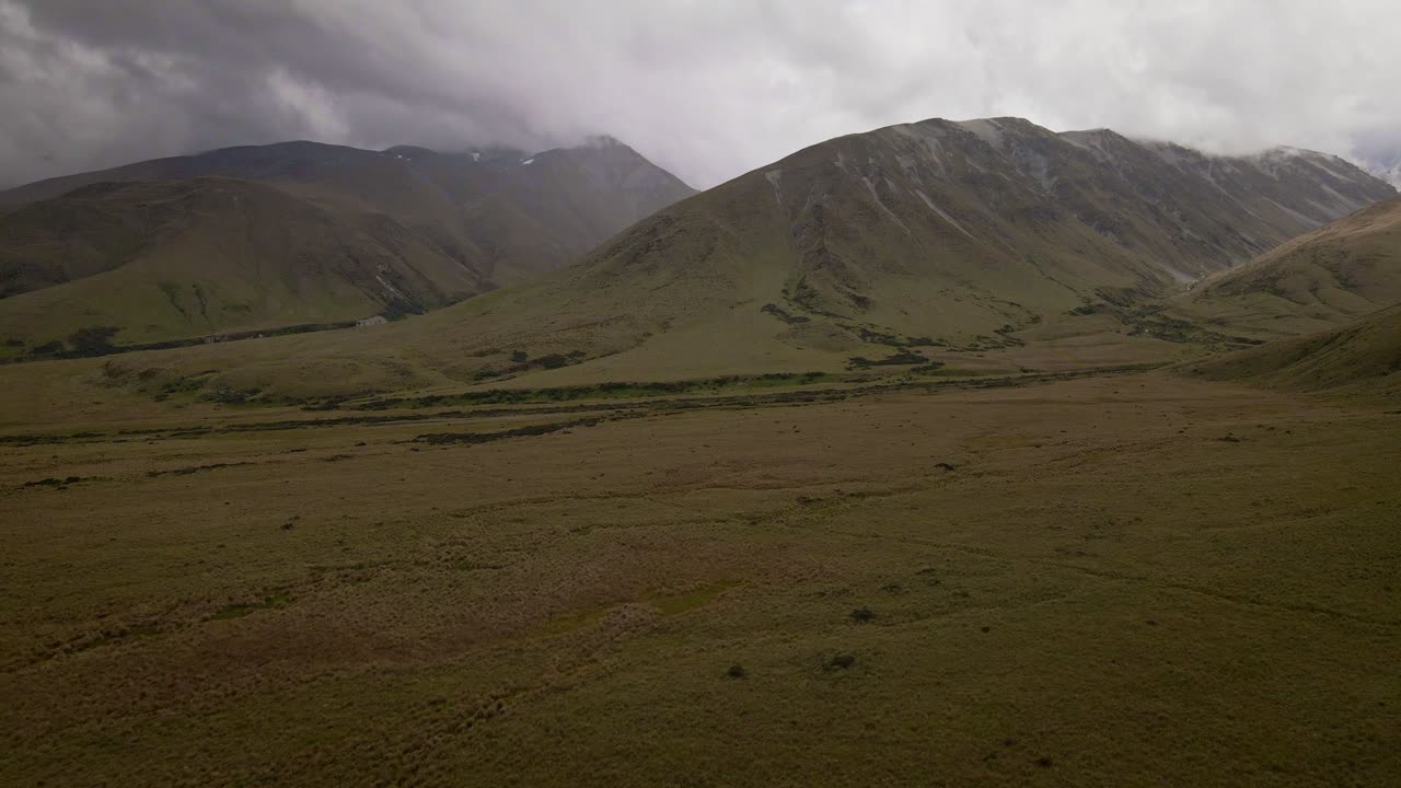 Vaste pianure di tussock ai piedi di una catena montuosa aspra che tocca pesanti nuvole temporalesche sopra
