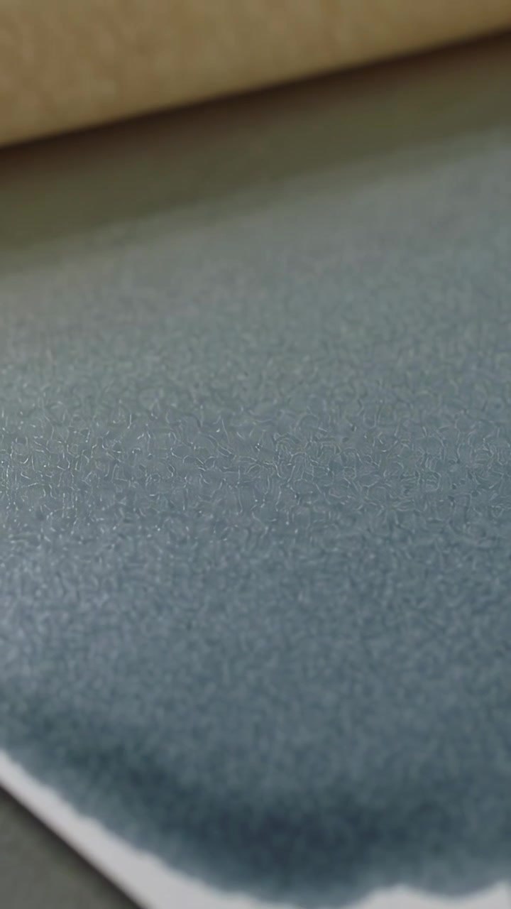 Vertical video: Lifting brayer moving across art table, revealing blue-gray wash on textured paper