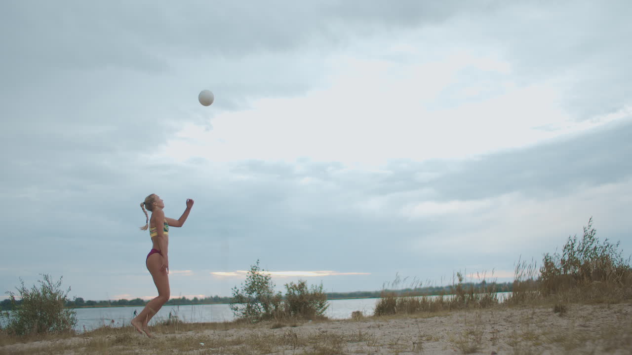 jugadora de voleibol de playa mujer está entrenando un servicio en la cancha en la naturaleza cámara lenta tiro de longitud completa