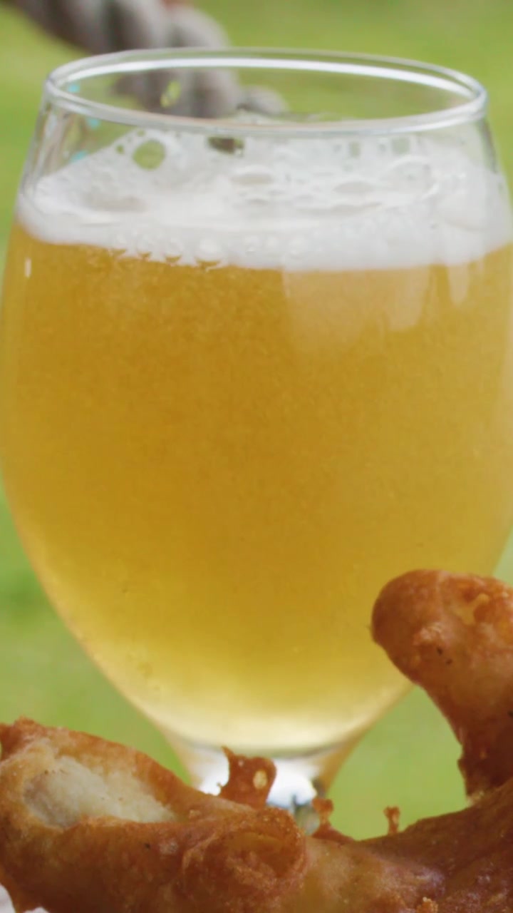 Un primo piano verticale di birra dorata versata in un bicchiere accanto a pesce fritto croccante.