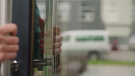 woman puts hand on iron handle opening modern glass door