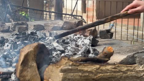 moving the burning charcoal to spread it and prepare a family barbecue