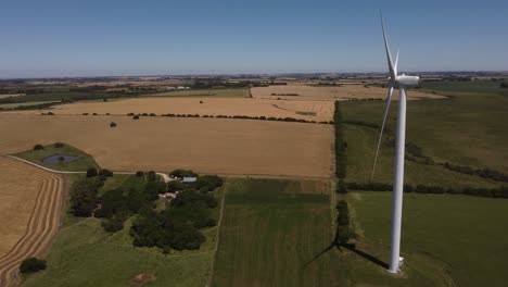 aerial orbiting shot of rotating wind turbine on countryside field during sunlight and blue sky - production of wind energy in nature
