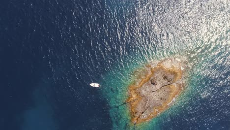 vista aérea superior pequeña isla de atolón con rocas y arena. agua azul clara y barco blanco desde un avión no tripulado.