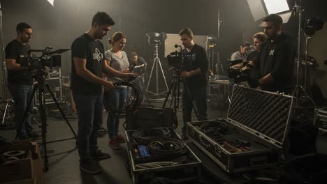 a behind-the-scenes look at film crews organizing equipment and setting up for a production in a studio with multiple cameras and lighting gear