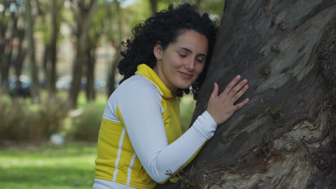 Jib up of a young activist woman smiling while hugging and stroking a tree with love in a park
