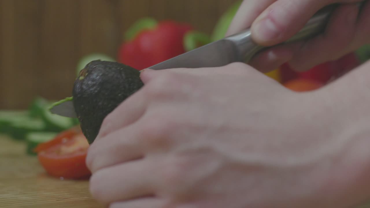 Young Man Messily Slicing Avocado in Half, Side View Closeup on Hands