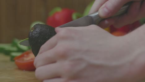 joven desordenadamente cortando aguacate por la mitad, vista lateral cerrada en las manos