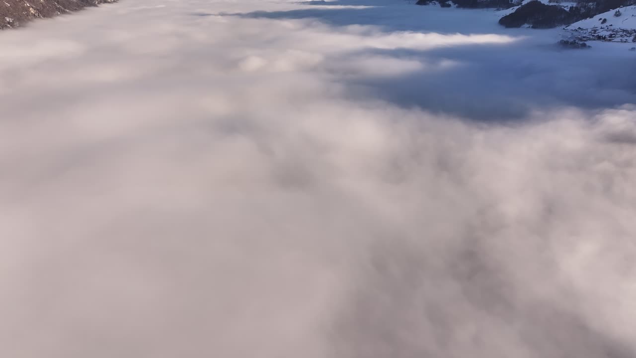 Revealing aerial view of a breathtaking sea of fog blanketing the stunning Wallensee in Switzerland, showcasing the transition from a cloud-filled vista to a picturesque winter landscape.