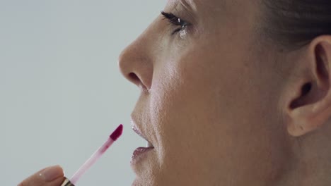 close up shot of a lady doing make up and putting on a red lip gloss