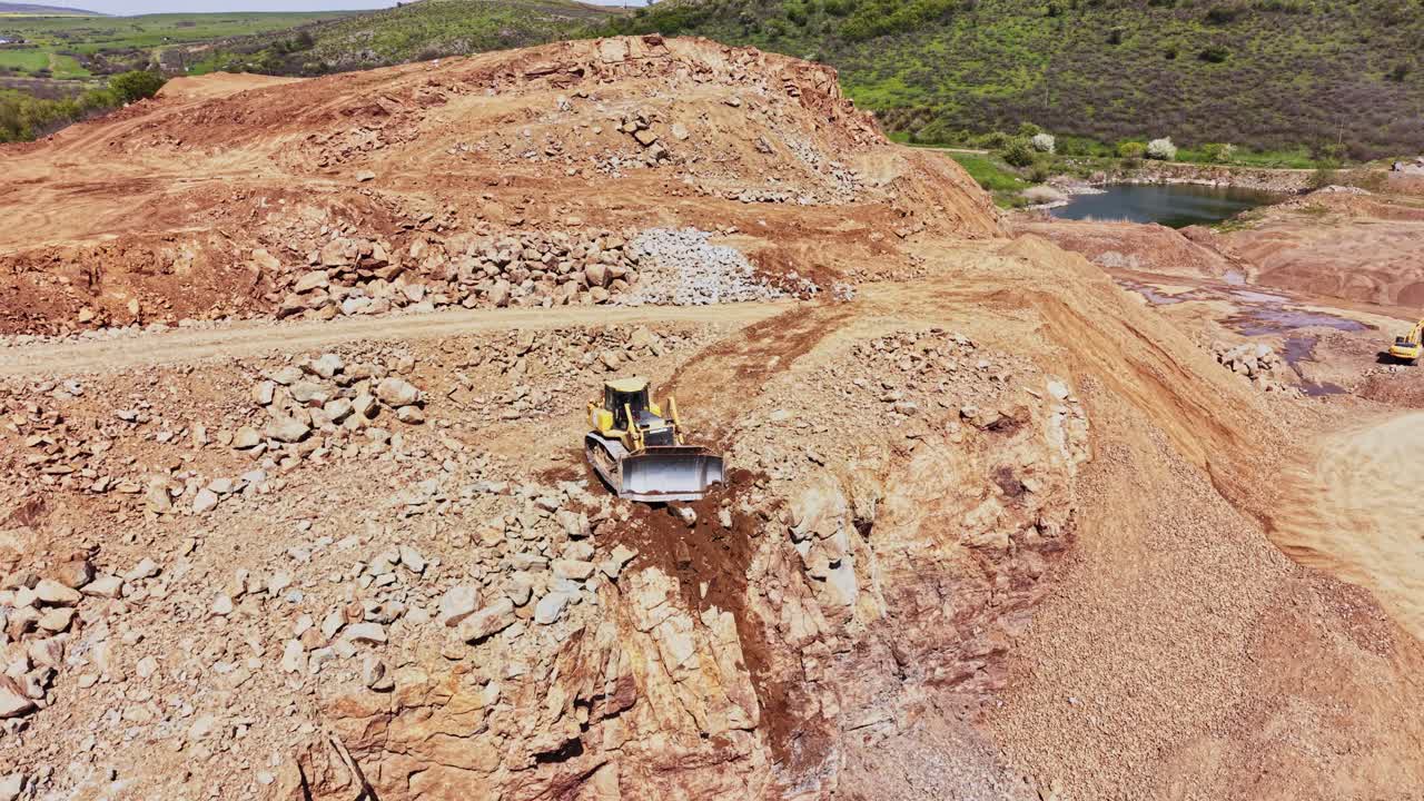 Máquinas pesadas operam em um canteiro de obras próximo a um corpo d'água durante o dia.