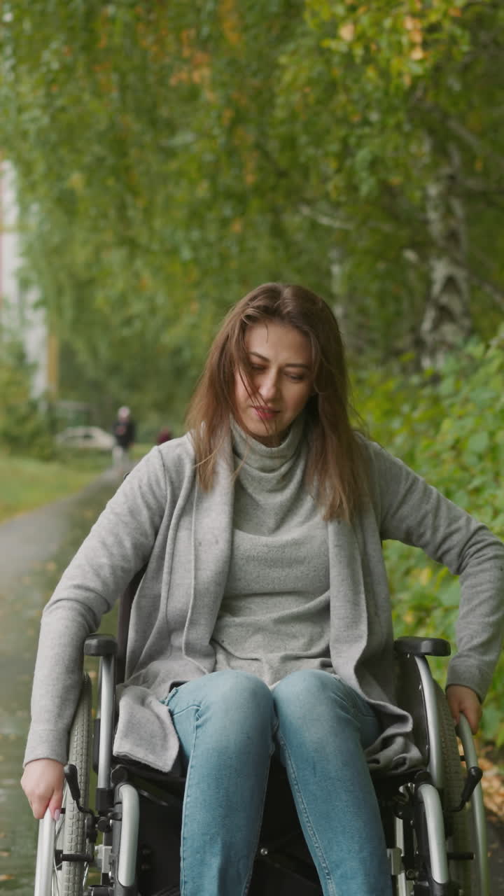Young woman with leg injury has free time during treatment in rehabilitation center. Smiling female in wheelchair enjoying nature on warm gloomy day with fresh air