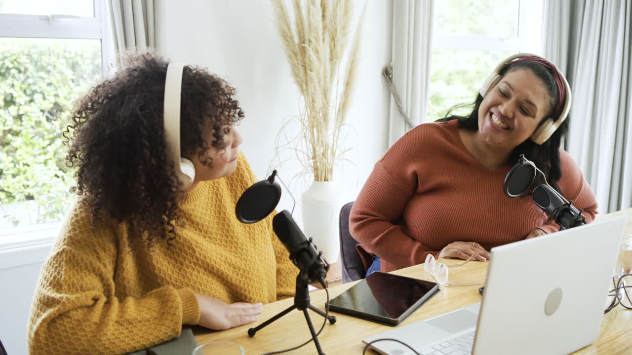 Due conduttori di podcast arrivano in studio, indossano le cuffie, regolano il microfono e discutono al laptop.