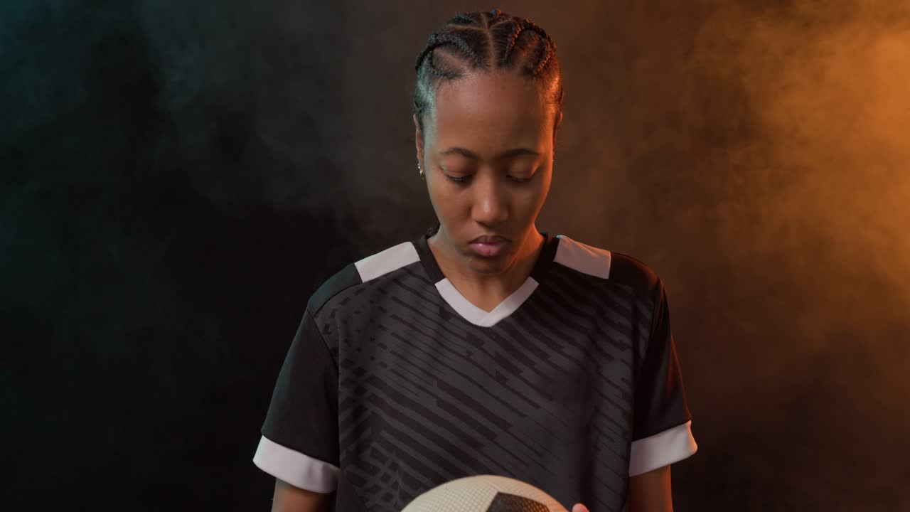 Donna africana in maglia nera tiene un pallone da calcio e si sistema mentre la telecamera zooma, incrociando lo sguardo in studio