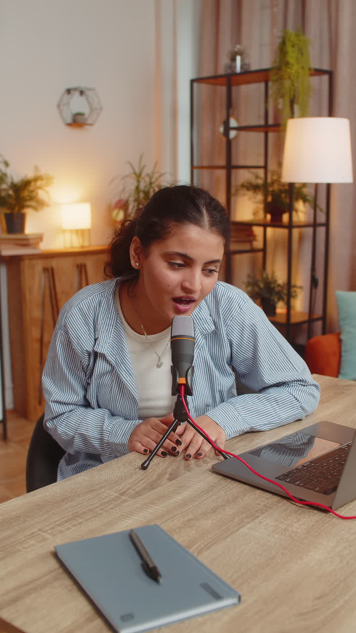 joven cantante bloguera india positiva que usa una computadora portátil mientras canta en el micrófono en la mesa