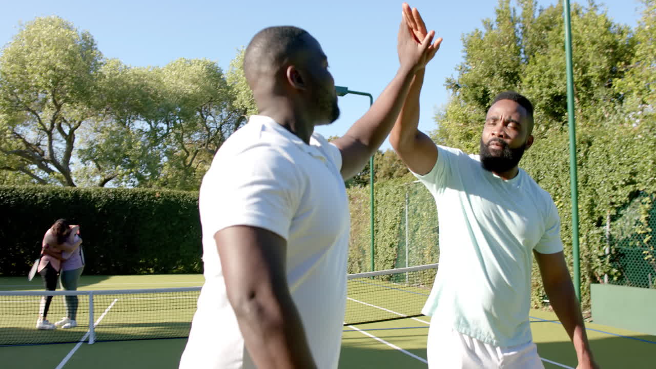 High-fiving, two friends celebrating on tennis court after successful game