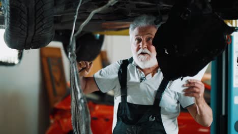 un anciano que trabaja en un servicio de automóviles escribe piezas defectuosas en un automóvil destrozado. taller de reparación de automóviles, servicio de automóvil, reparación.