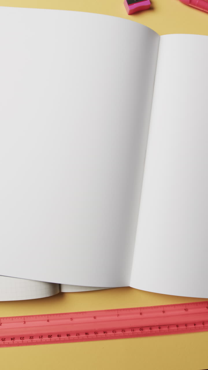 Vertical video of overhead view of open notebooks on beige background, in slow motion