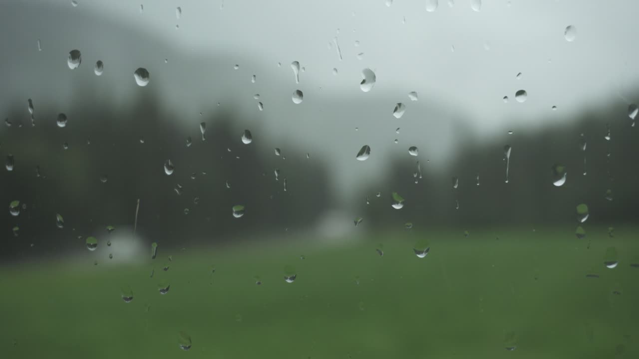 Rain drops on window glass with blurry nature background, static close up shot