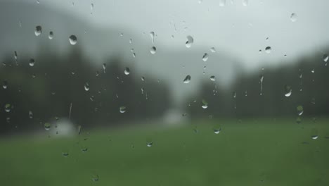 Gotas-De-Lluvia-En-El-Cristal-De-La-Ventana-Con-Fondo-De-Naturaleza-Borrosa,-Toma-Estática-De-Primer-Plano