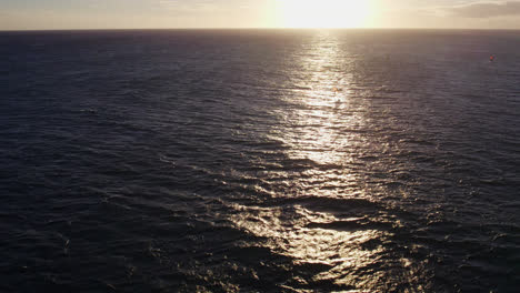 drone footage circling a kite surfer at a distance on the pacific ocean honolulu hawaii as the sun reflects across the calm ocean waves as it prepares to set