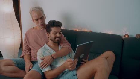 happy gay couple watching tablet on couch