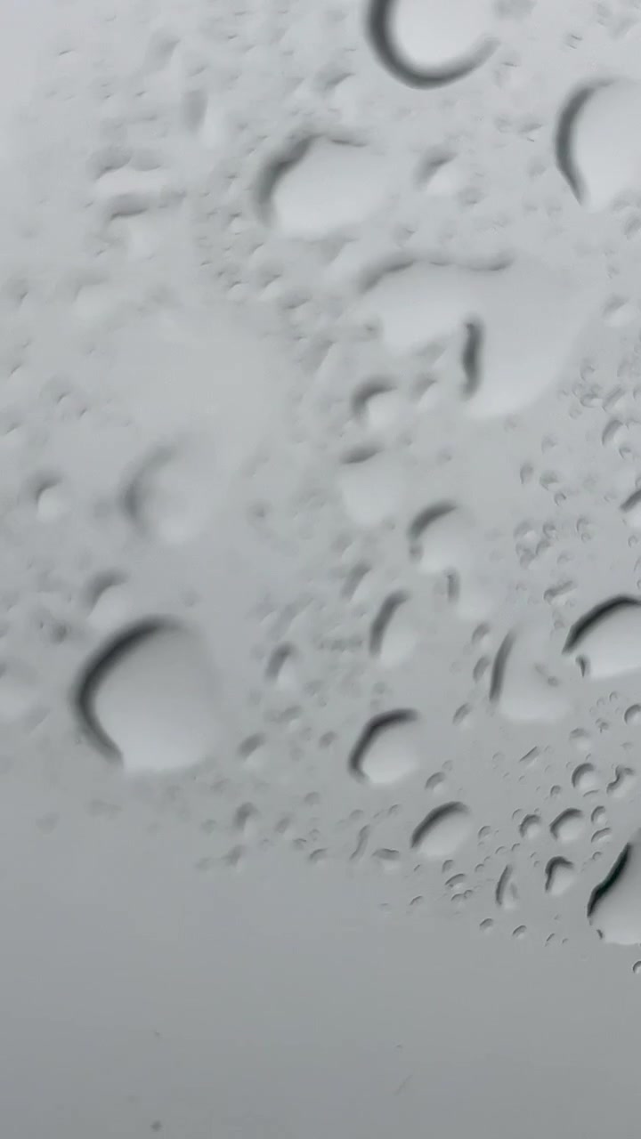 Abstrakt makrobilde av vanndråper som glir ned en glassoverflate under et regnvær. Minimalistisk filmatisk bakgrunn for vær, velvære eller stemningsfull historiefortelling.