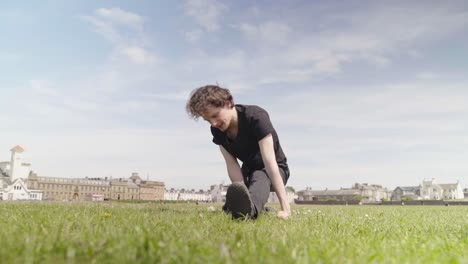 Young-adult-male-is-stretching-and-warming-up-on-grass-outside-daytime