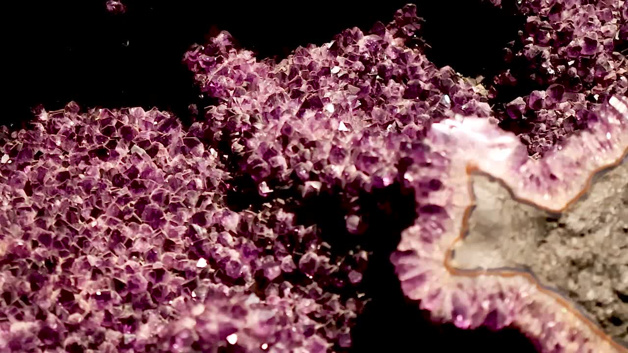 Veduta macro dettagliata di cristalli di quarzo viola scintillanti e texture di roccia geologica su sfondo nero.