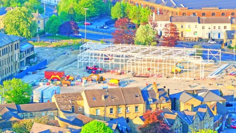 huddersfield city centre revealing active construction site with steel framework being assembled, construction vehicles, nearby victorian houses, trees, and local roads, drone static shot
