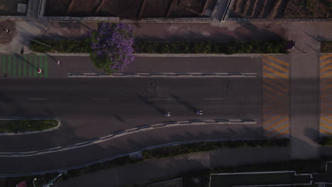 Aerial-top-down-view-pedestrians-on-sidewalk-by-main-road-with-cars-and-two-cyclist-in-traffic