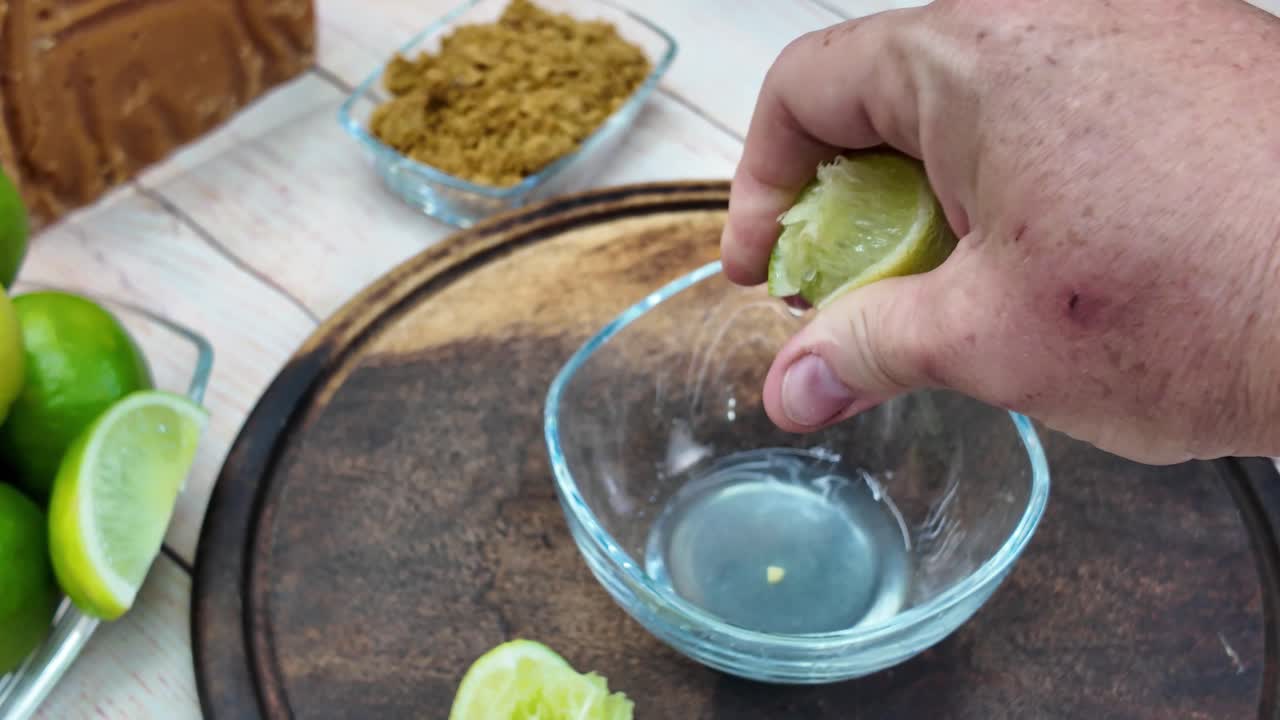 hands-on process of squeezing fresh lime juice into a small clear glass bowl. Green fruit and clear liquid, essential acidic component for a refreshing beverage