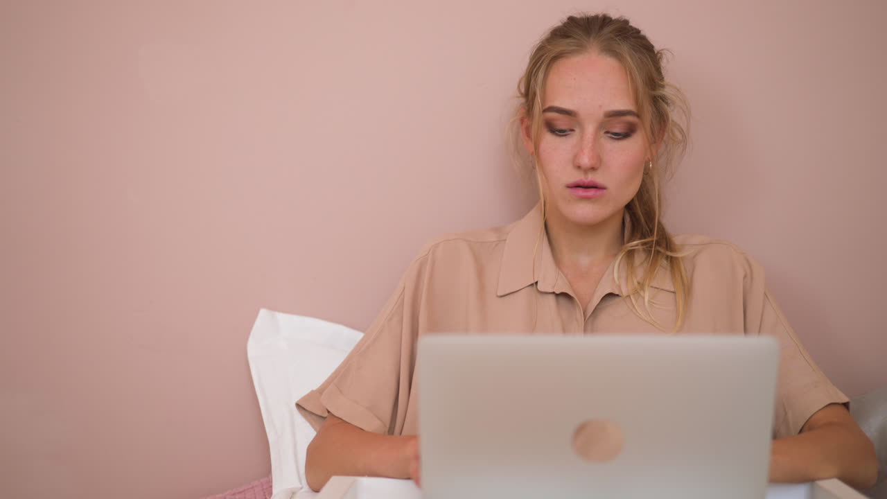 una joven estudiante escribe un diploma a través de una computadora portátil sentada en la cama