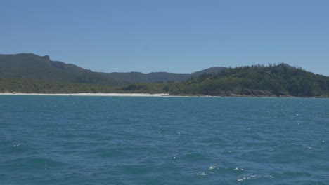 Rippling-Coral-Sea-With-View-Of-Densely-Forested-Island-In-Background