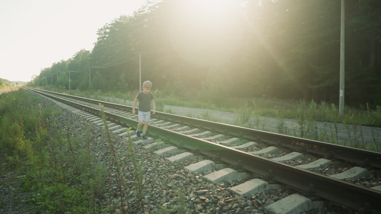 kid in casual outfit playfully jumping on rail sleeper along quiet railway surrounded by nature, with golden sunlight casting warm glow on forest background