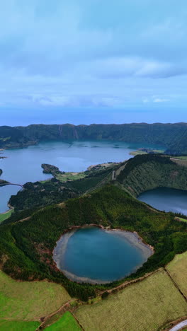 craters of sleeping volcanoes filled with lakes. picturesque village is located on the waterfront. panorama of the azorean islands. top view. vertical video.