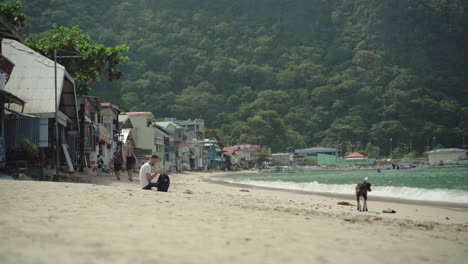 tourists enjoying and relaxing in the white sand beach in el nido, philippines with green trees and calm sea - wide shot