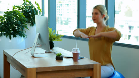 Female-executive-doing-exercise-on-exercise-ball-at-her-desk