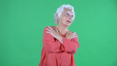 retrato de una mujer mayor mirando a la cámara con una expresión conmocionada y asustada en el rostro y cruzando los brazos sobre el pecho. abuela de cabello gris con blusa roja en la pantalla verde en el estudio.