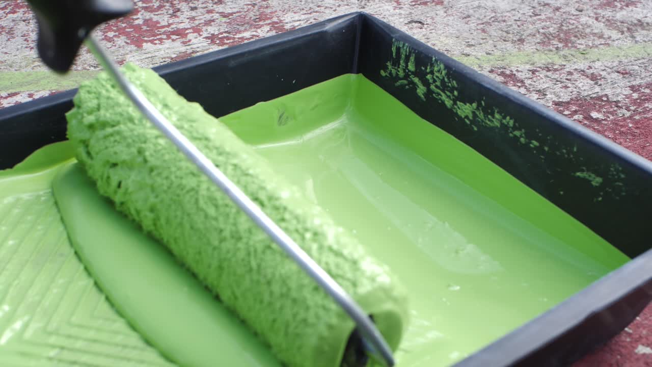 el arte de pintar: un primer plano en cámara lenta de un artista sumergiendo un rodillo en pintura verde vibrante