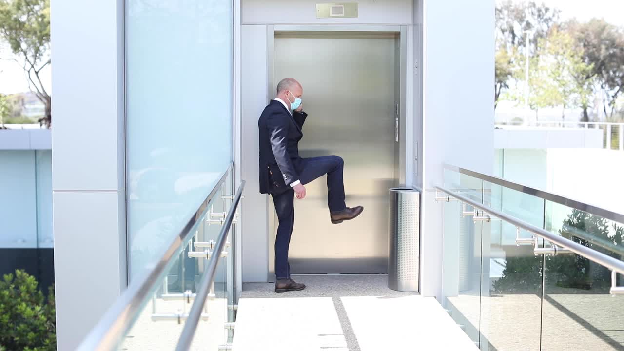 un modelo lanzó una máscara que usa un hombre patea un botón de ascensor durante el brote epidémico de coronavirus covid19