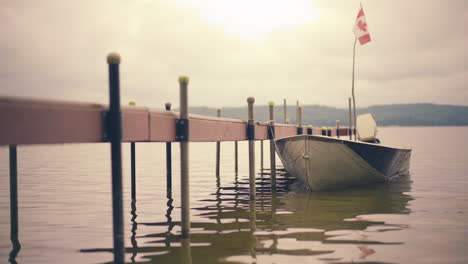 Kleines-Boot,-Das-Während-Der-Goldenen-Stunde-In-Einem-Ruhigen-See-Mit-Wunderschönem-Landschaftshintergrund-4k-Prores-Am-Holzsteg-Festgebunden-Ist