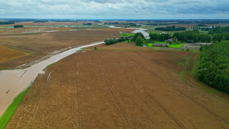 Vast-agricultural-fields-with-waterlogged-areas-and-a-farmstead-in-the-distance,-aerial-view