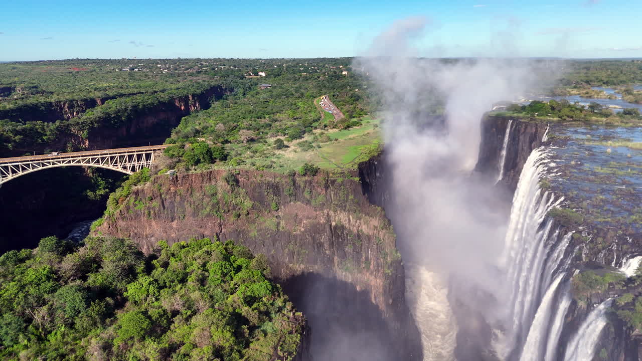 Aerial view of Victoria Falls with powerful waterfall plunging into gorge, mist rising above lush green forest, dramatic natural wonder and iconic travel destination in Africa