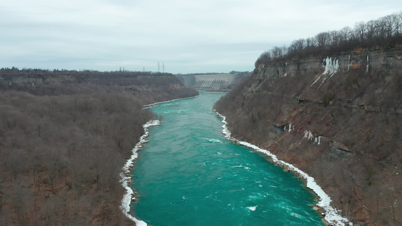 Aerial shot of river flowing through gorge towards hydro electric dam